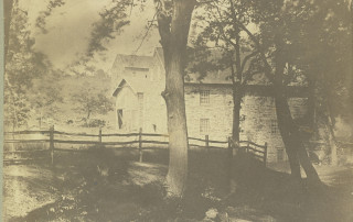 Very old black and white photograph of Peirce Mill with the barn in the distance. Handwritten caption