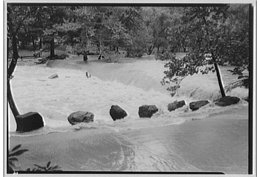 An old black and white photograph of the dam at Peirce Mill, completely overwhelmed by flood water.