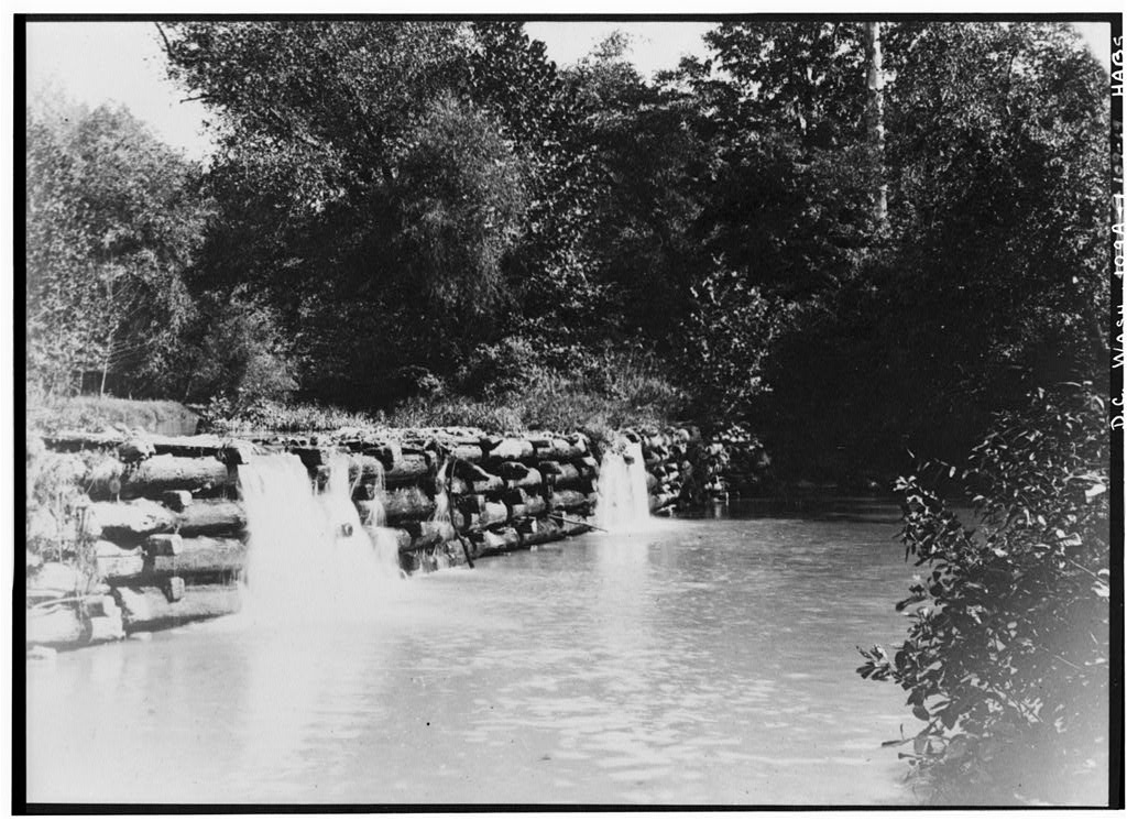 Old black and white photograph of a dam made of stacked logs