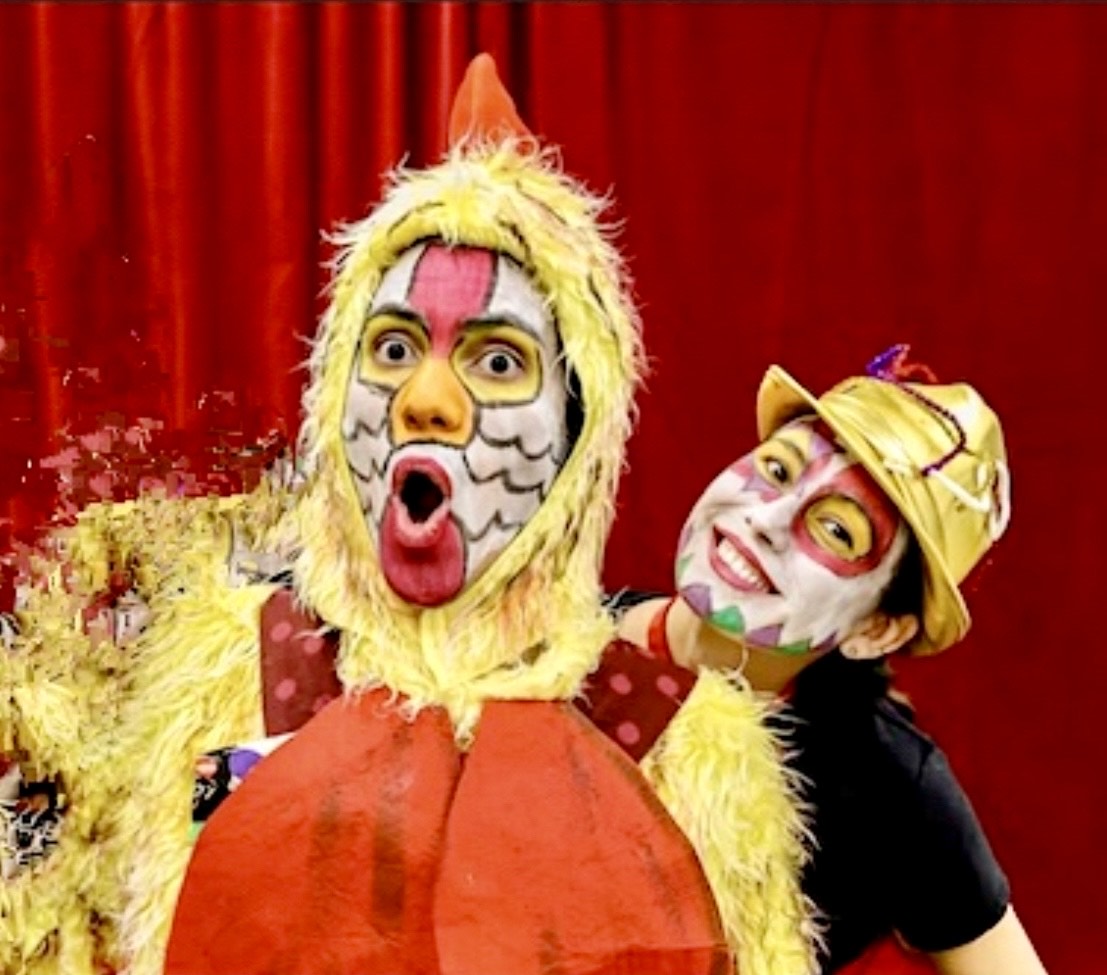 Two smiling actors with elaborate face paint. One is wearing a chicken suit.