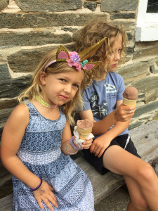 Two girls sitting in front of a stone building eating ice cream.