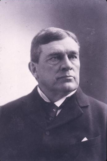 Black and white photograph of a serious man in a jacket and tie