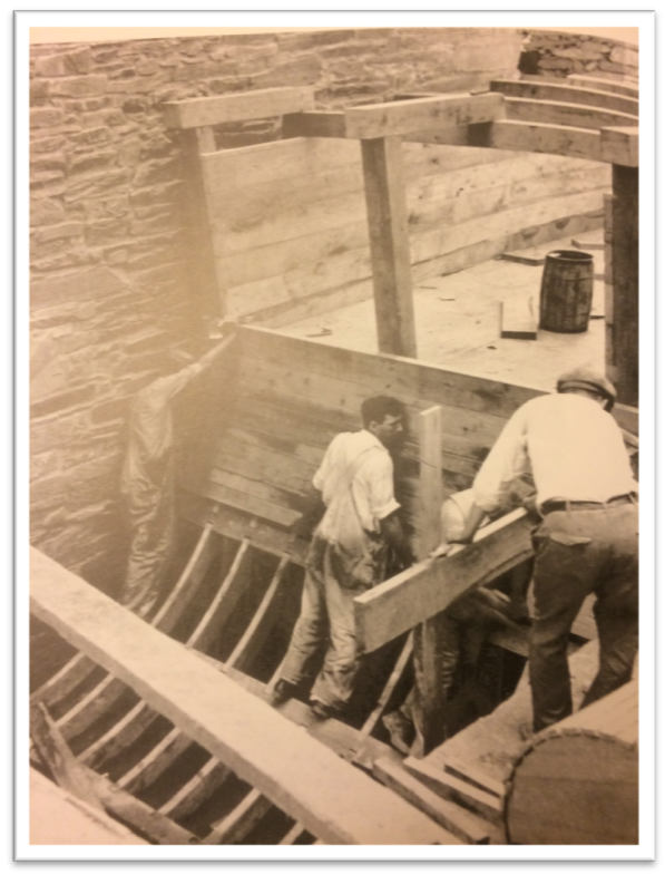 Workers rebuild a wooden waterwheel next to an old stone building