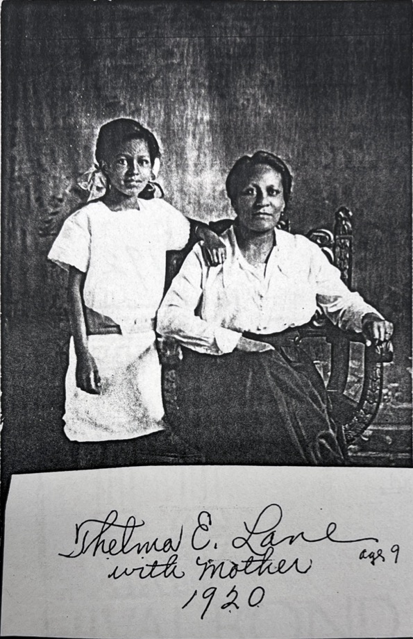A young girl in pigtails stands next to her mother