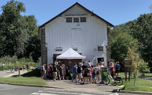 2022 Ice Cream Demo in Front of Barn People gather under a tent in front of a big white barn