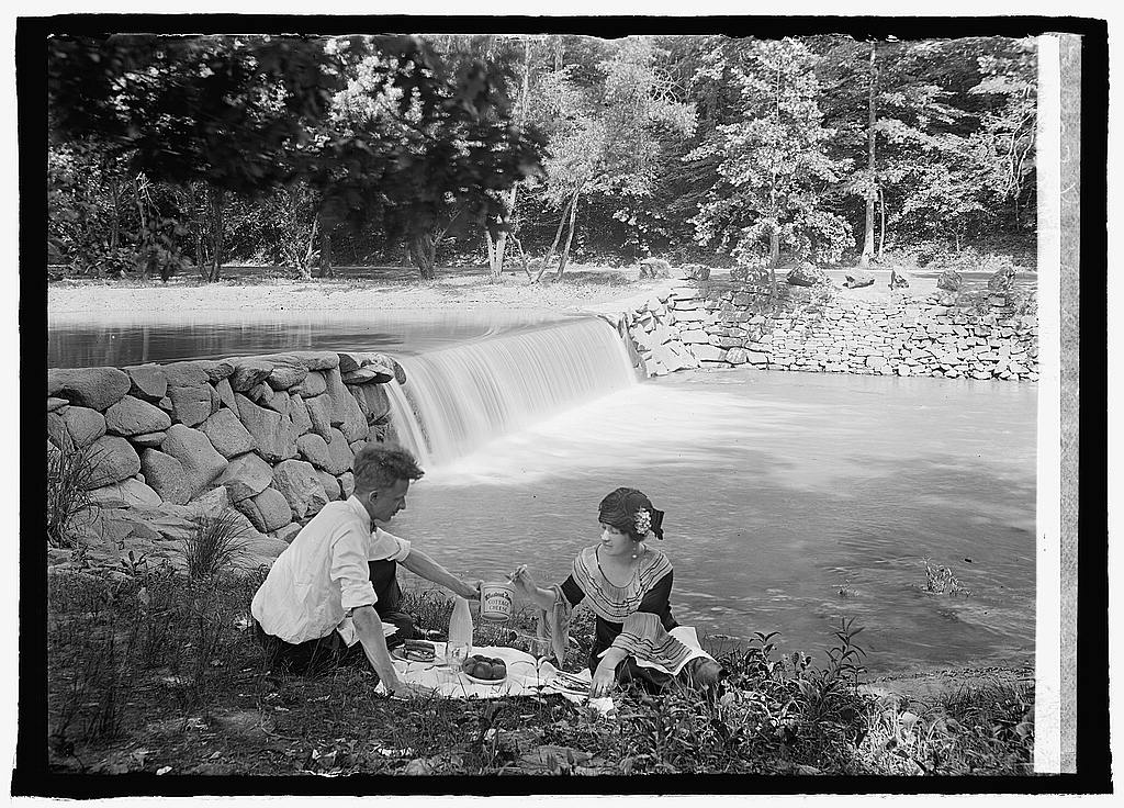 An early-twentieth century photograph of a man and woman picnicking in front of a waterfall.