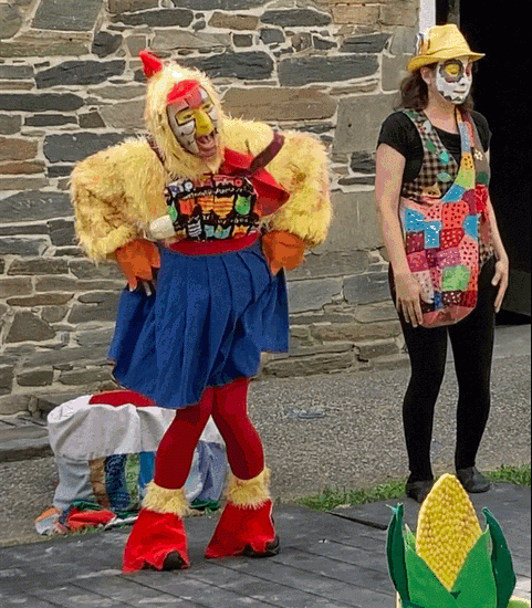 A chicken and actor in colorful dress perform for children