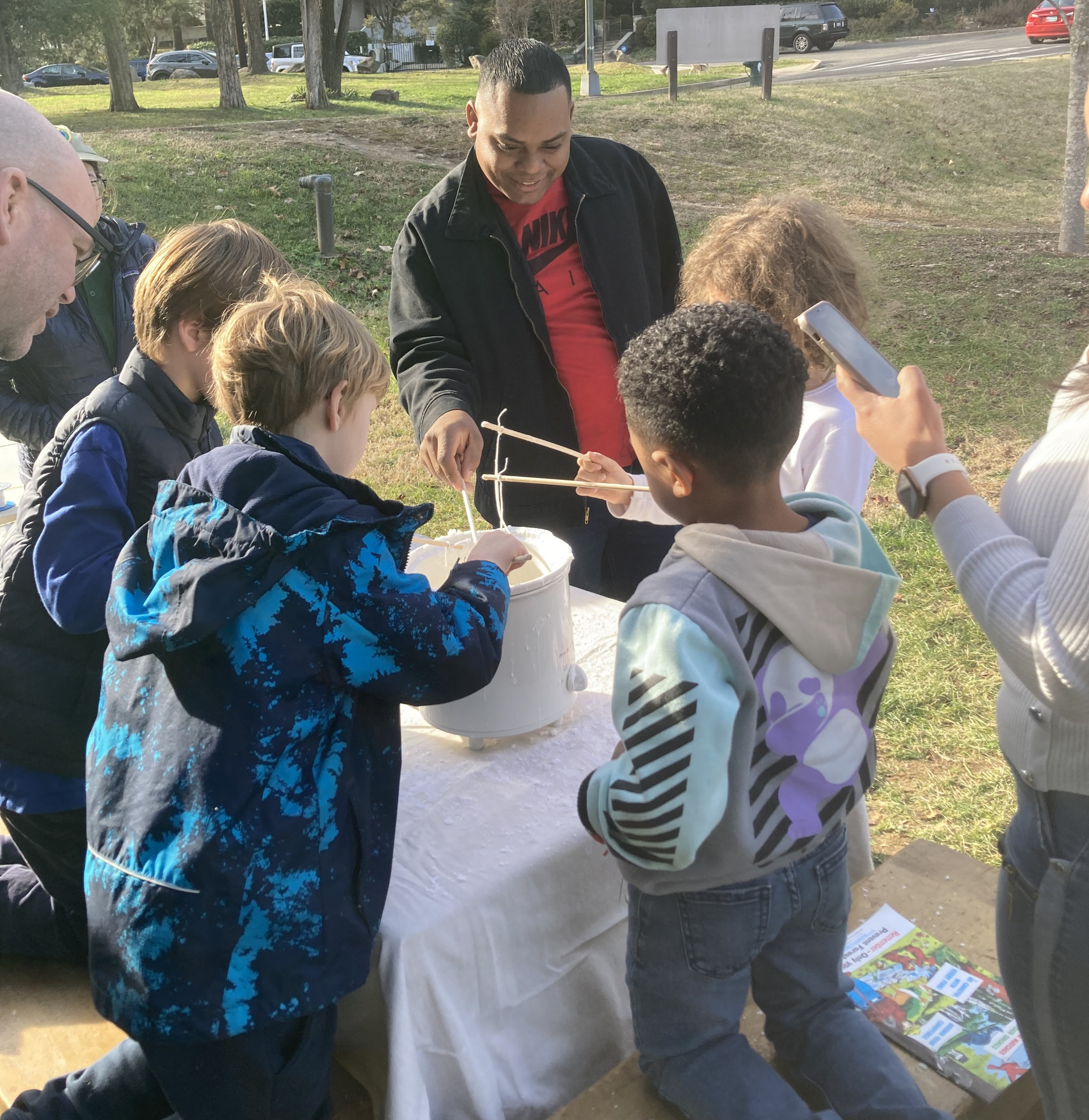 People stand around a crock pot dipping string into wax to make candles.