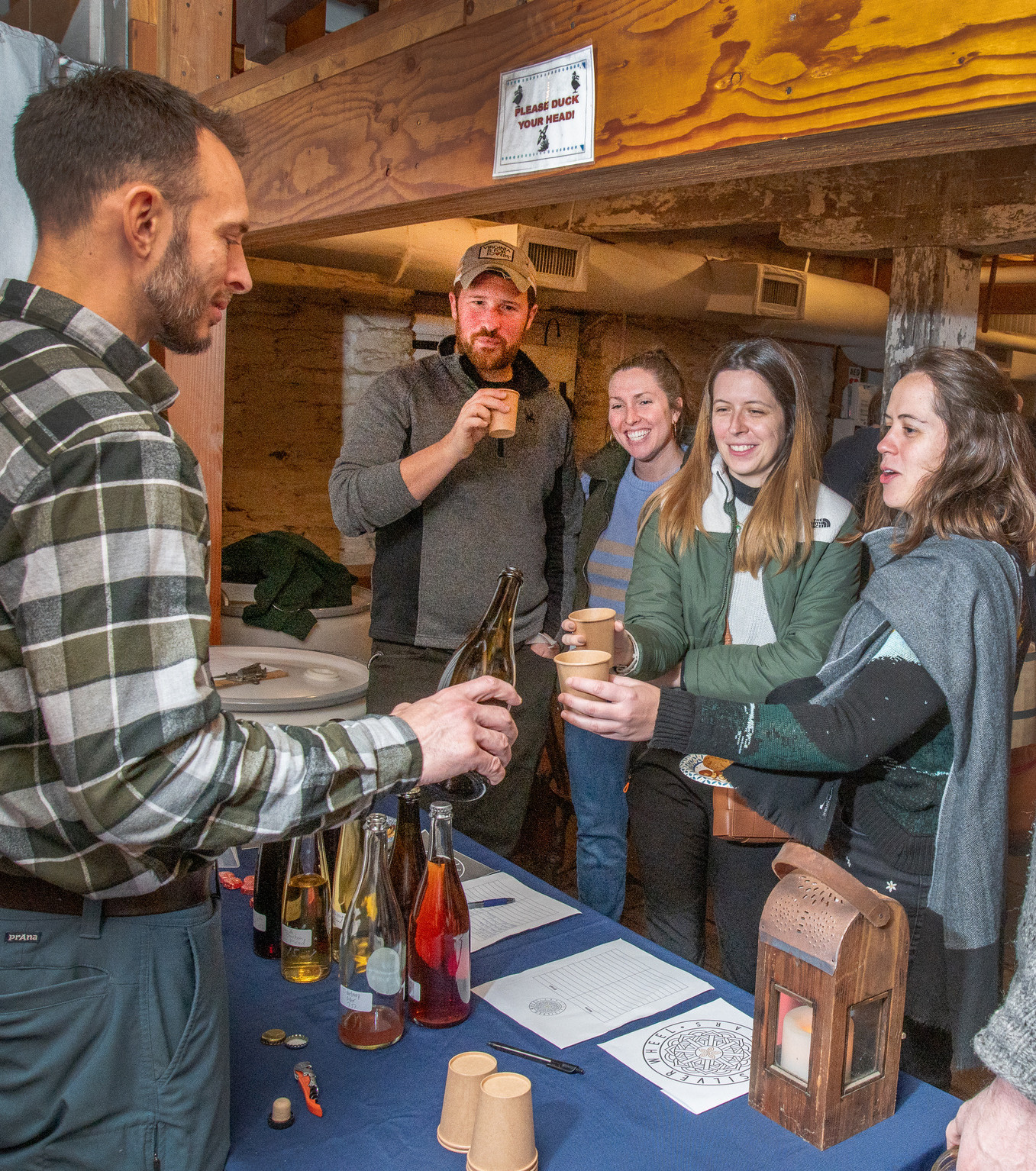 A group of people standing at a table with a variety of ciders on it.
