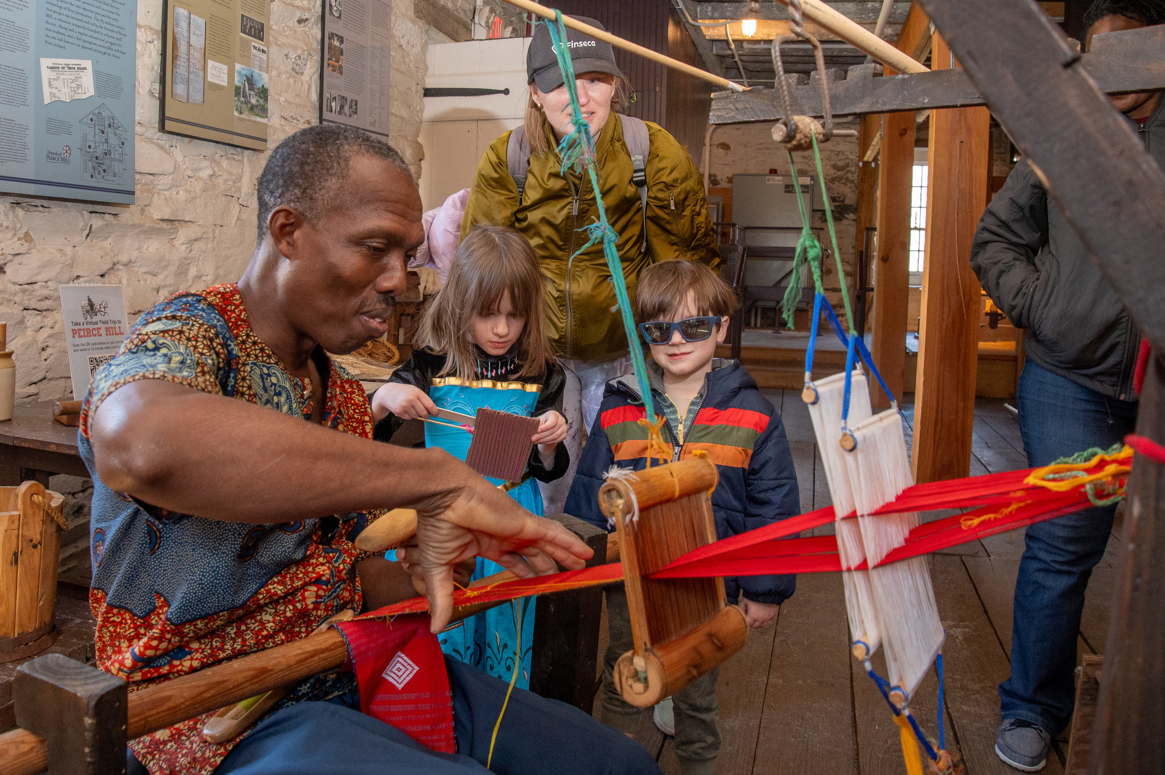 A man weaves kente cloth while a family looks on