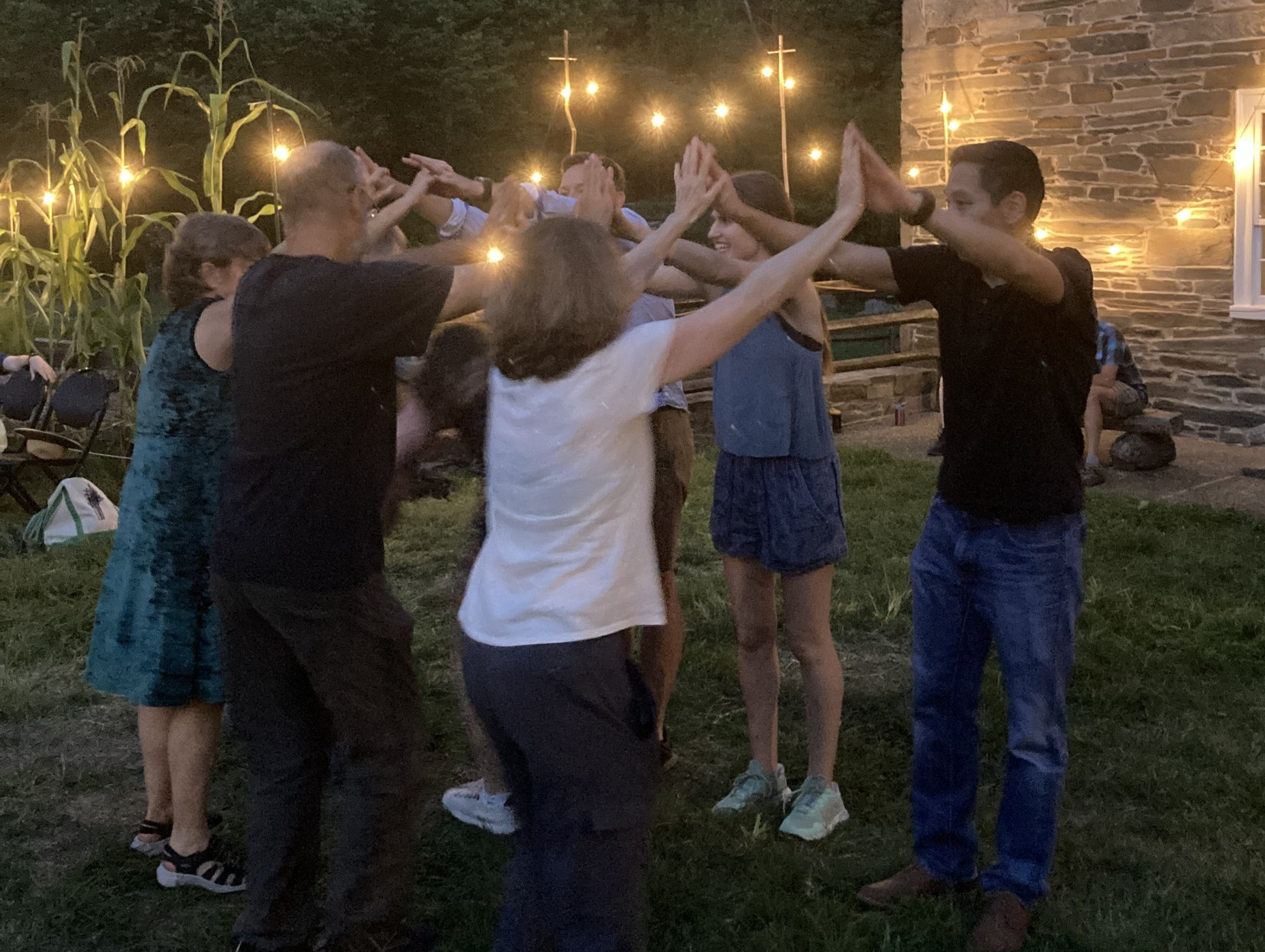 People join hands to form an arch under string lights in front of an old stone building