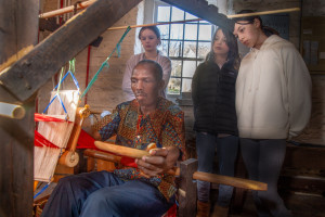 Man uses a loom to weave Kente cloth. 