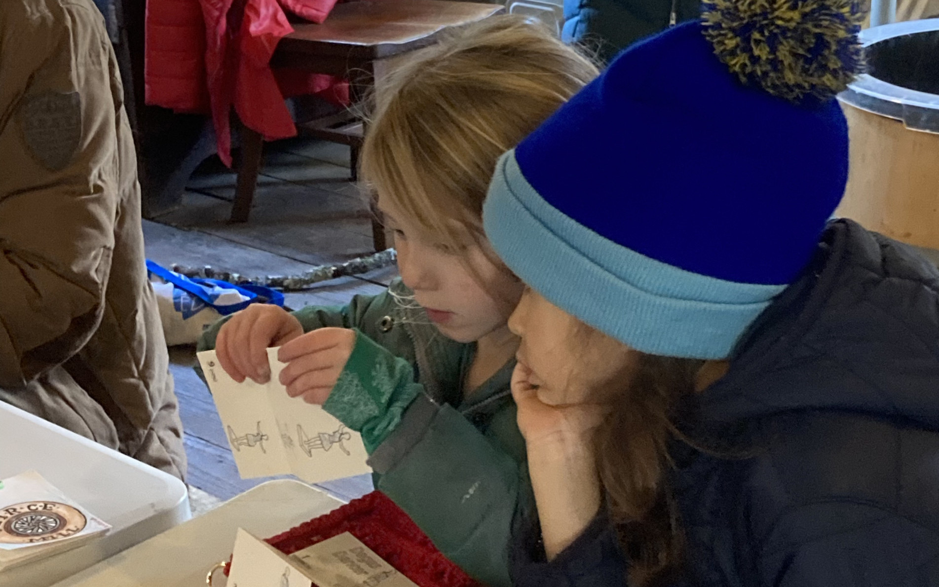 Two children in winter clothes make crafts inside an old building.