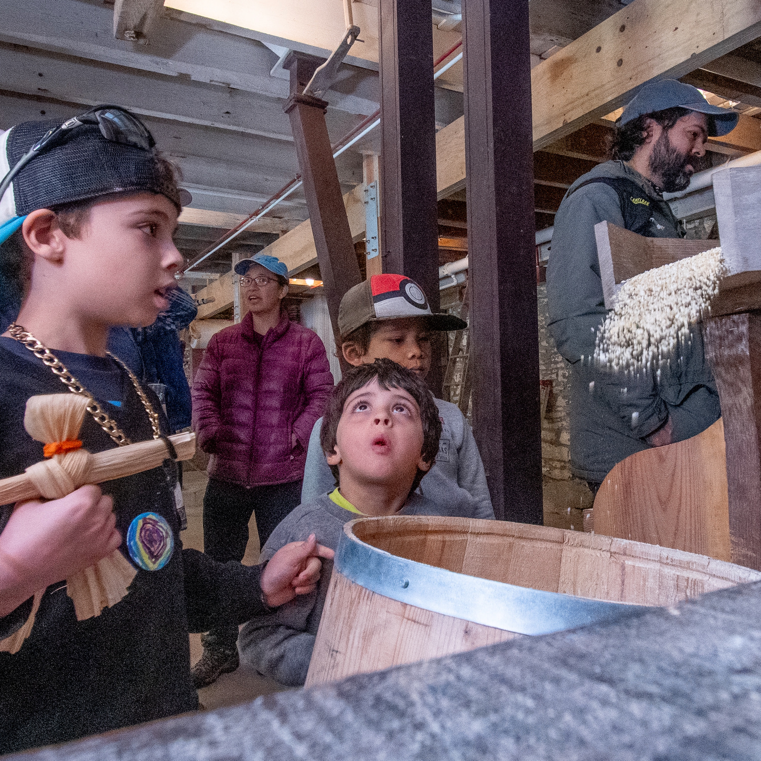 A group of children watch corn meal being ground at an old mill