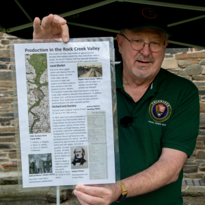 A man holds an interpretive sign in front of a stone building