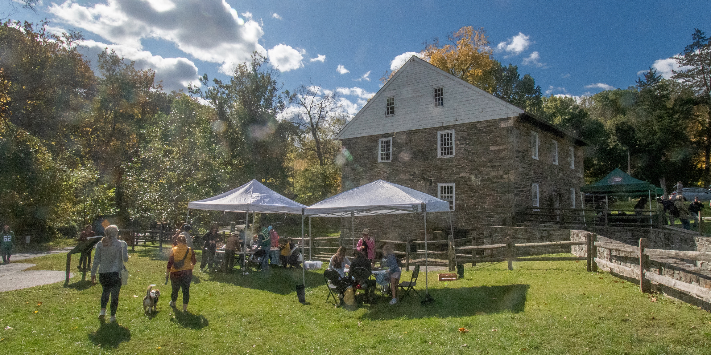 People walk toward tents sent up next to an old mill on a fall day