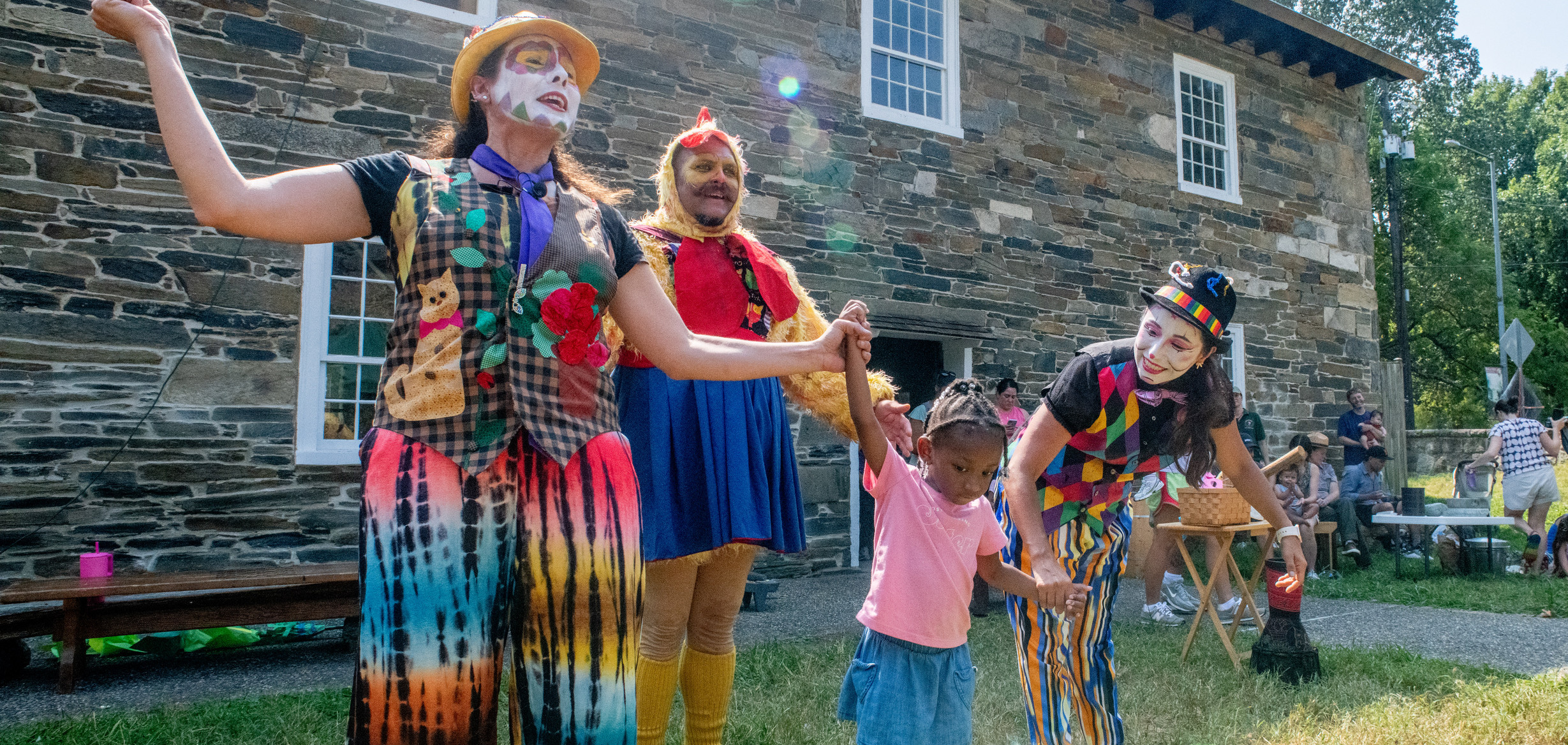 Costumed characters perform with a small child in front of an old mill