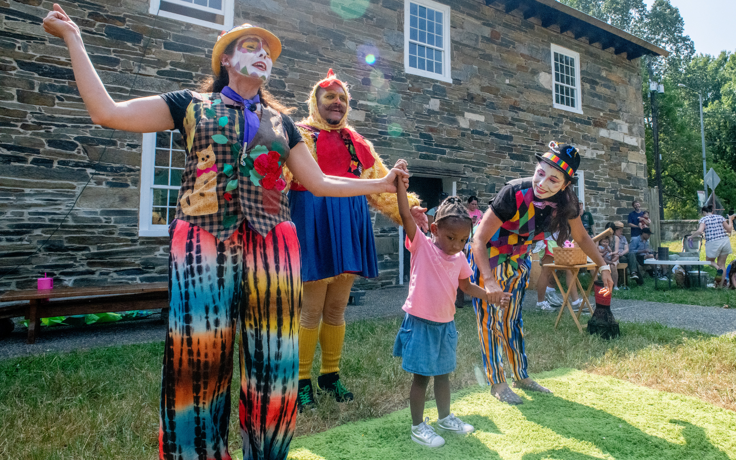 Costumed characters perform with a small child in front of an old mill